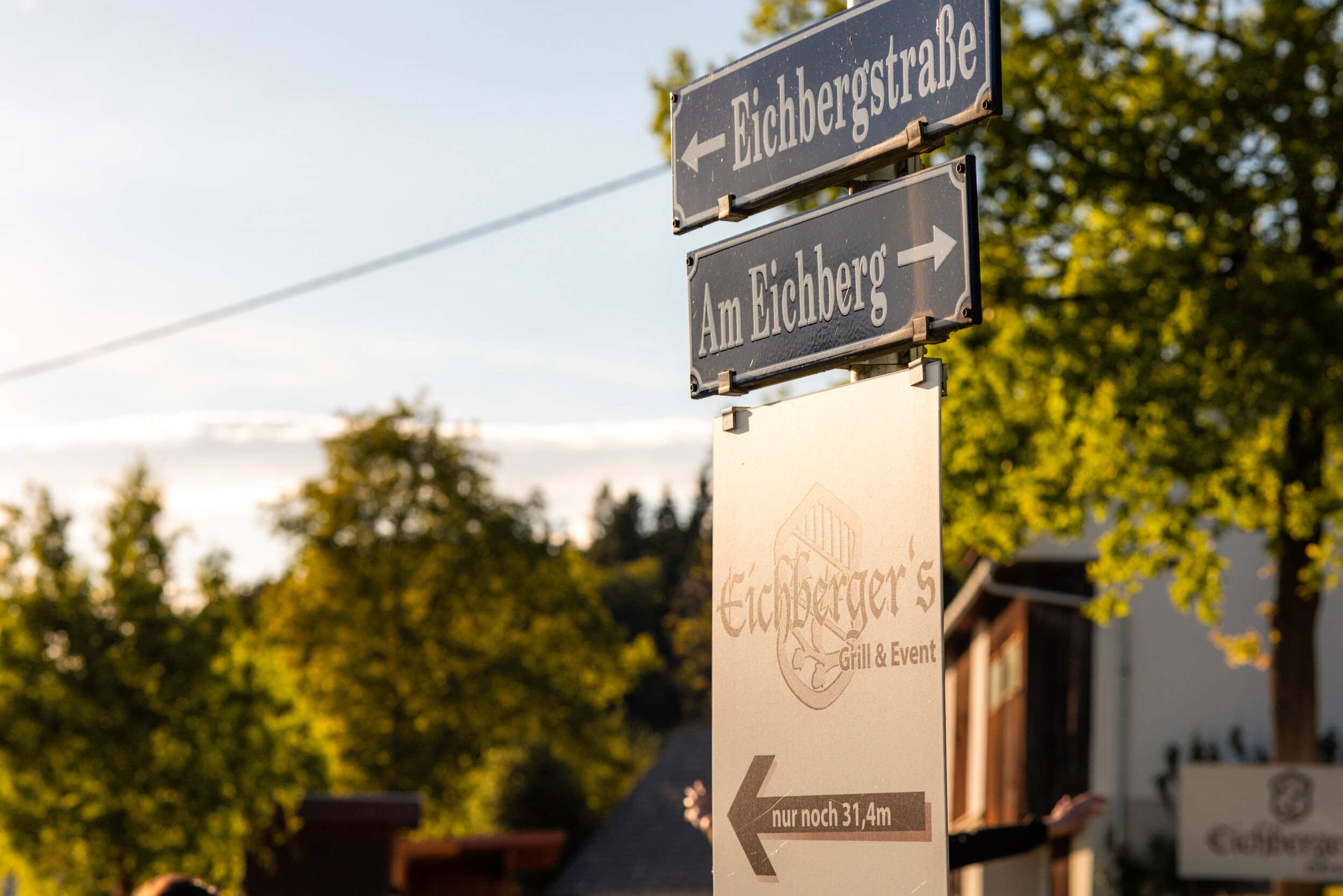 Straßenschilder bei Eichberger's Grill in der Natur mit Bäumen und Himmel.