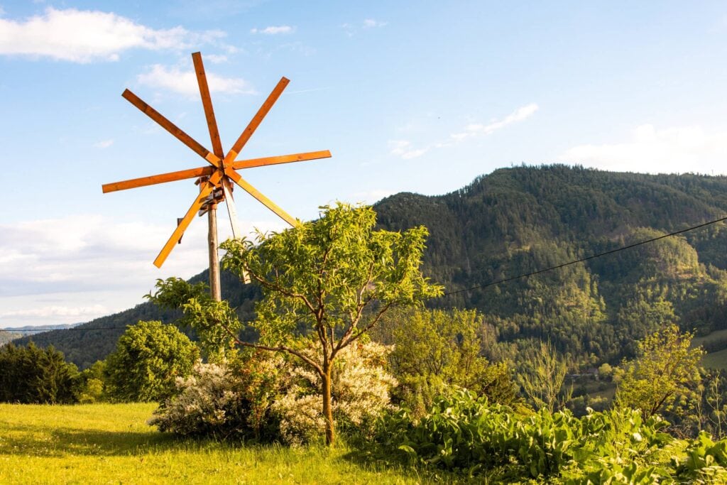 Landschaft mit Windmühle, Bäumen und Hügeln im Hintergrund.