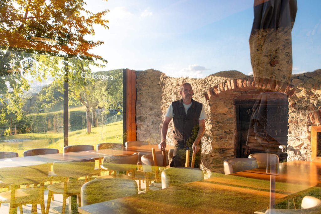 Mann bei Grill-Event in rustikalem Gasthaus mit Holzofen und Naturblick.