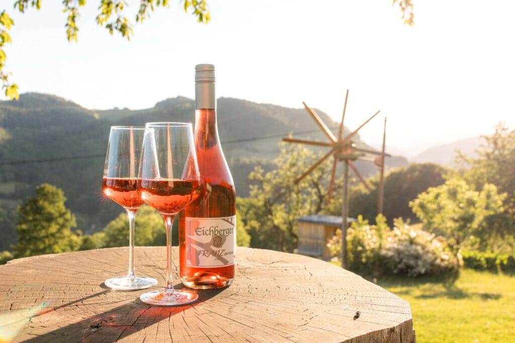 Roséwein und zwei Weingläser auf Baumstamm mit Bergblick im Hintergrund.