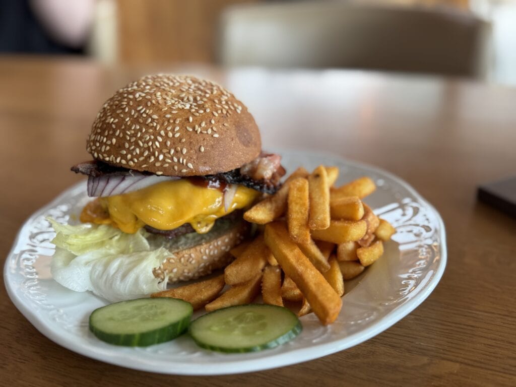 Burger mit Käse, Speck, Zwiebeln, Gurkenscheiben und Pommes.